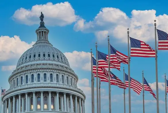 The iconic U.S. Capitol building is prominently displayed, flanked by multiple American flags fluttering in the breeze.