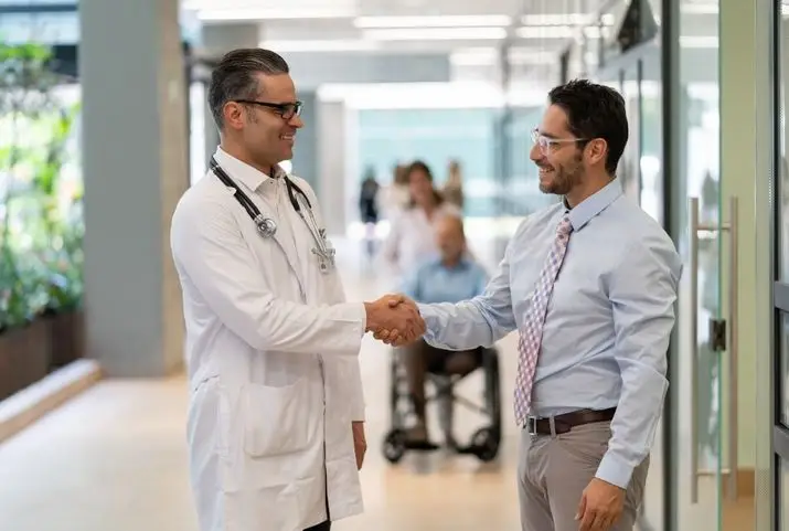 Two doctors shaking hands in a hospital hallway, symbolizing collaboration and professionalism in healthcare.
