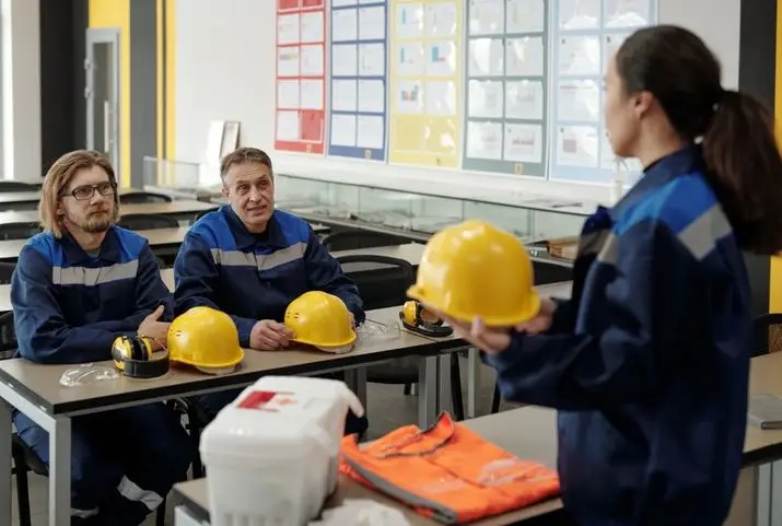 A group of three people in hard hats gathered around a table, with one person offering a training to the other two people