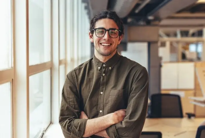 Portrait of a smiling young man in an office setting, dressed in business attire, exuding a professional demeanor.