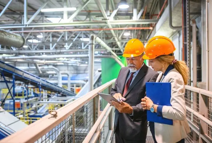 Two individuals in hard hats examining a tablet, likely discussing a project or construction plans.
