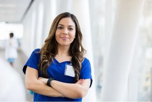A healthcare worker standing in a hallway with her arms crossed