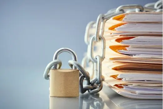 A stack of compliance documents with a padlock and chain around it
