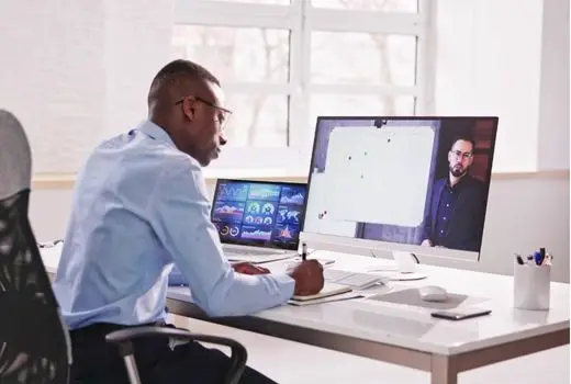A man seated at a desk with two computer monitors displaying various content.