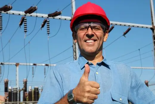 Man in red hard hat with thumbs up stands in front of electrical field